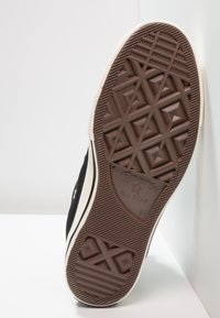 Semelle de baskets en toile noire avec une semelle extérieure en caoutchouc marron affichant un motif de traction en losanges et formes géométriques. Comprend le logo "Converse All Star".