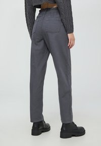 Pantaloni grigi dalla vestibilità comoda con vita elastica, due tasche posteriori e gambe affusolate, abbinati a stivali neri con plateau.