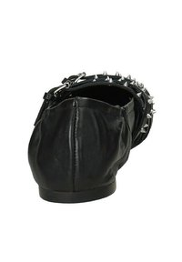 Scarpa piatta in pelle nera con punta arrotondata, decorata con spuntoni in metallo argentato attorno al tallone, superficie testurizzata e suola liscia.