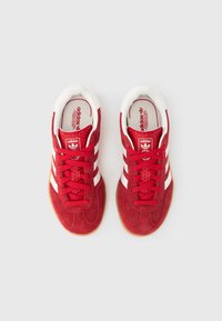 Röda träningsskor i mocka med vita ränder och matchande snören, utrustade med en vadderad insida och en sula i gummigummi.