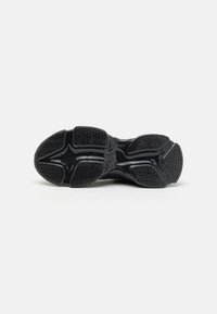 Semelle de chaussure en caoutchouc noir avec des motifs texturés, présentant un design central lisse et des crampons surélevés pour l'adhérence et la traction.