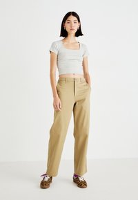 T-shirt corto grigio chiaro con scollo quadrato, abbinato a pantaloni beige a gamba dritta. Gli accessori includono scarpe con stampa animale e lacci viola.