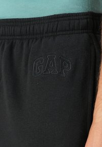Μαύρες φόρμες από μαλακό ύφασμα, με ελαστική μέση και κεντημένη τη λέξη "GAP" σε πιο σκούρο τόνο στο μπούστο.