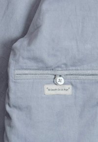 Helehall kangas sileda tekstuuriga, millel on turvaline tasku, valge silt kirjaga „Till Death Do Us Part” ja nööbiaksent.