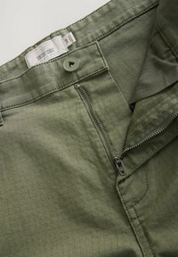 Zielone spodnie o teksturowanym wykończeniu, z zapięciem na guzik i zamkiem, oraz metką oznaczoną "NEAT Durable Goods."