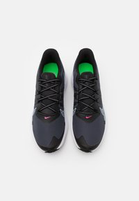 Schwarze Sportschuhe mit Mesh-Obermaterial, grünen Innensohlen, pinken Akzenten und schwarzen Schnürsenkeln. Verfügen über eine weiße Sohle mit strukturiertem Muster.