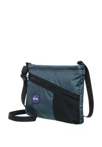 Messenger-väska i mörk teal nylon med en svart panel, med en diagonalt placerad dragkedjeficka och en justerbar rem. Logotypmärke synligt.