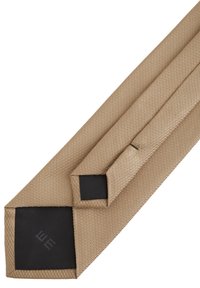 Smėlio spalvos tekstūruotas vyriškas kaklaraištis su juodu audinio pamušalu ir mažu etiketu ant nugarinės kilpos.