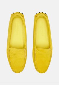 Gule ruskind loafers med sømdetaljer og sorte hardware aksenter på overdelen. Blød, tekstureret finish med runde tæer.