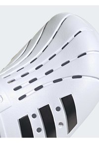 Scarpa sportiva bianca con tomaia textured e dettagli neri, feritoie di ventilazione e suola in gomma resistente.