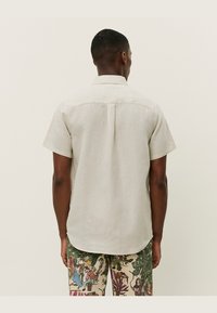 Camisa de manga corta en color beige claro, hecha de lino. Cuenta con un dobladillo recto, un pliegue en la espalda y un cuello sencillo. Diseño casual con un ajuste relajado.
