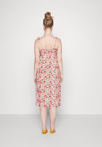Vestido midi floral com alças finas, tecido leve com padrões em vermelho e verde, textura suave e um corpete justinho com saia rodada.