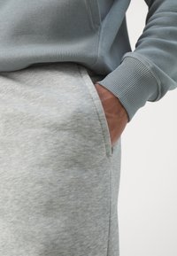 Lys blå genser med ribbestrikkede mansjetter, kombinert med grå joggebukser med lomme og et mykt, teksturert stoff.