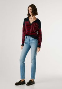 Tumestriibuline sviiter punaste horisontaalsete triipudega, V-kaelus ja soonikkoes varrukad. Kombineeritud helesiniste kitsaste teksade ja mustade mokassiinkingadega.