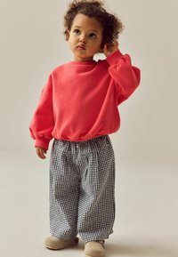Felpa corallo con polsini a costine, pantaloni in gingham bianco e nero, e scarpe beige. I pantaloni hanno una vestibilità comoda e una cintura elastica.