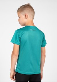 Teal athletic shirt with short sleeves, smooth texture, and a crew neck. Features a logo on the upper back, paired with black shorts.
