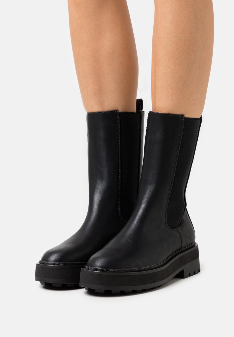 Black ankle boots with a smooth leather finish, elastic side panels, chunky tread sole, and a pull tab at the back.