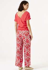Top de cuello en V color coral con mangas enrolladas, combinado con pantalones de pierna ancha que presentan un patrón floral rojo y blanco y un acabado texturizado.