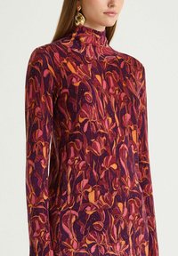 Pullover a manica lunga con collo alto di colore viola con motivo floreale in rosa e arancione. Texture morbida con silhouette aderente.