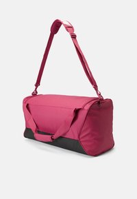 Roze sporttas met een rechthoekige vorm, voorzien van een bovenrits, twee handgrepen en een verstelbare schouderband. Zwarte onderkant voor duurzaamheid.