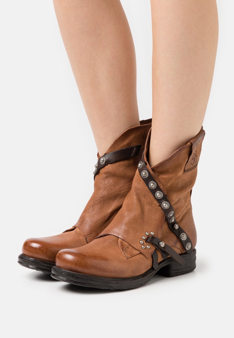 Stivali alla caviglia in pelle marrone con accenti in metallo, design piegato e tacco nero basso. Presentano una cintura laterale e un dettaglio con il marchio.