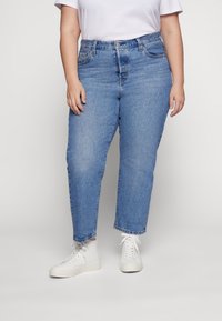 Jeans rectos de color azul claro con un acabado ligeramente desgastado, cinco bolsillos y un dobladillo deshilachado, combinados con zapatillas deportivas blancas de caña alta.