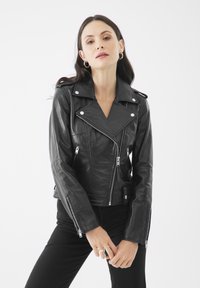 Giacca da motociclista in pelle nera con accessori in argento, zip asimmetrica, rever larghi e silhouette aderente. Texture liscia, lunghezza corta.