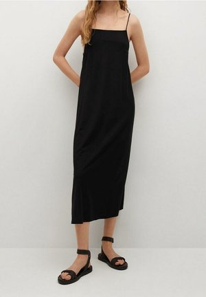 Robe midi sans manches noire avec de fines bretelles, tissu lisse et légère évasement à l'ourlet. Associée à des sandales noires tressées.
