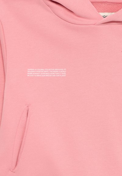 Sudadera con capucha rosa que presenta un bolsillo tipo canguro y tejido texturizado. Texto impreso en blanco que describe la misión medioambiental de la marca.