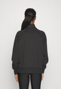 Svart tröja med hög krage, raglanärmar och ribbade mudd. Tillverkad av strukturerad tyg, med en avslappnad passform och minimalistisk design.