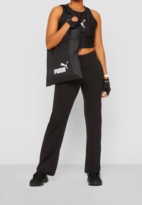 Černý sportovní outfit zahrnující crop top a rozšířené kalhoty, s černou taškou Puma a bezprstovými rukavicemi, vše v ladících barvách.