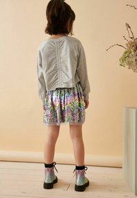 Pullover grigio con retro arricciato, abbinato a una gonna di paillettes multicolor e stivaletti iridescenti alla caviglia con lacci neri.