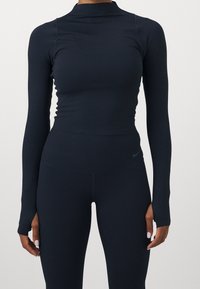 Haut de sport à manches longues bleu marine avec un col montant, design sans coutures et matériau extensible, associé à des leggings côtelés taille haute assortis.