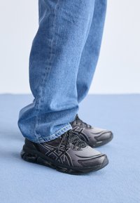 Svarta träningsskor med en stilren design, ovandel i mesh och en strukturerad sula. I kombination med blå denimjeans som är något kortade vid vristerna.