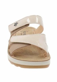 Sandali beige con una superficie lucida, caratterizzati da cinturini incrociati, chiusure in velcro e una soletta imbottita; un logo accentuato sul cinturino sinistro.