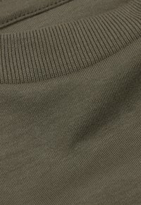 Olivově zelená pletená tkanina s žebrovanou texturou podél okrajů. Detailní pohled na měkký materiál a detaily šití.