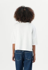 White cropped t-shirt with short sleeves, smooth texture, and a round neckline, paired with high-waisted blue denim jeans.