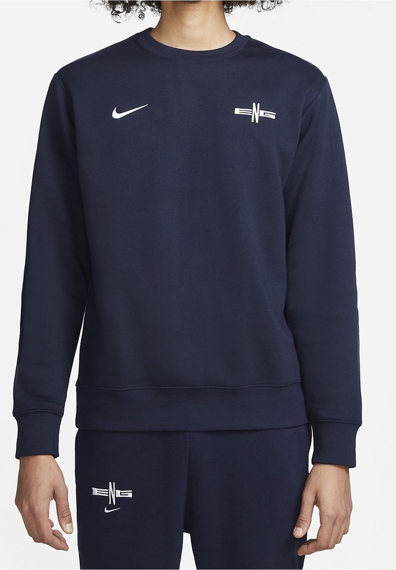 Personne portant un sweat-shirt bleu marine à manches longues et un pantalon assorti avec les logos Nike et le marquage blanc "ENG" sur la poitrine et la cuisse.