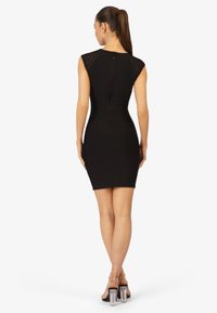 Zwarte bodycon jurk met kapmouwen, gestructureerde stof en een rits aan de achterkant. Gecombineerd met zwarte sandalen met doorzichtige hakken.