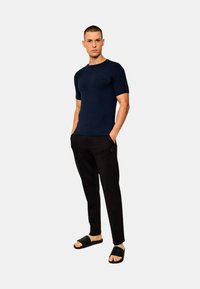 T-shirt a maniche corte navy, slim fit, abbinato a pantaloni neri con dettagli in logo e ciabatte nere con finitura texturizzata.
