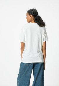 Camiseta blanca de algodón de manga corta, con un corte relajado y escote redondo. Combinada con jeans de mezclilla azul de cintura alta.