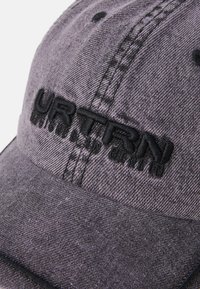 Căciulă de baseball din denim gri, cu logo-ul brodat "URTRN" în negru, având o margine curbată și o coroană structurată, detalii din țesătură texturată.
