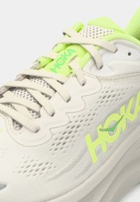 Λευκό αθλητικό παπούτσι με λάιμ πράσινο διακοσμητικό στοιχείο, διαθέτοντας υφασμένη επάνω επιφάνεια, ορατές οπές και αντίθετο λογότυπο στο πλάι.