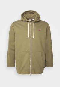 Sudadera con cremallera en verde oliva, con cordones blancos, bolsillos frontales y un pequeño logo rojo en el lado izquierdo del pecho.