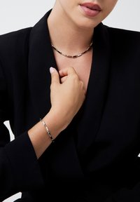 Set di collana e bracciale in argento realizzato con pezzi di metallo collegati. La collana poggia sul collo, mentre il bracciale decora il polso, entrambi con un design elegante.