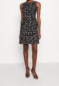 Černé bezramínkové šaty se rozptýleným vzorem pastelových teček, těsně přiléhající korzet, rozšířená sukně a délka ke kolenům. Hladká látka.