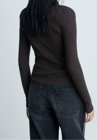 Haut marron côtelé à manches longues associé à un jean large taille haute gris foncé. La texture est douce et la coupe ajustée à la taille.