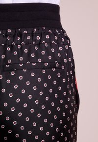 Svart tygbyxor med små vita och röda blommönster, elastiskt midjeband och en diskret sidficka. Slät textur och lättvikt.
