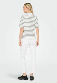 Top a righe con maniche corte in bianco e blu navy, caratterizzato da una vestibilità rilassata. Abbinato a jeans bianchi e scarpe slip-on nere. Design minimalista.