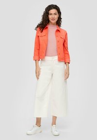 Korallefarbene Jeansjacke, rot-weißer gestreifter Oberteil, weiße weite Hosen und weiße Sneakers, mit Knöpfen und ausfransenden Saumdetails.